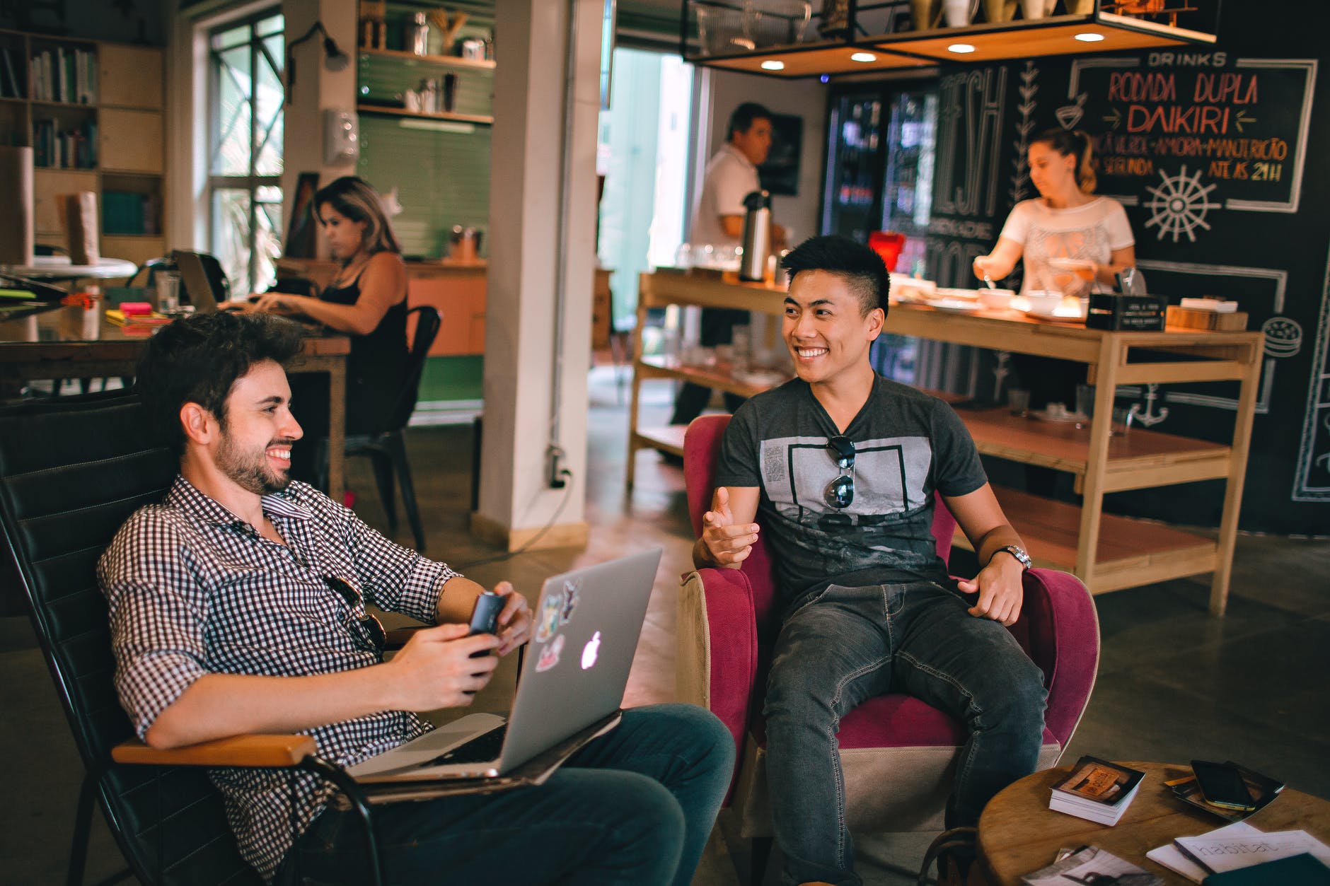 Two men sit in a café and chat, smiling.
