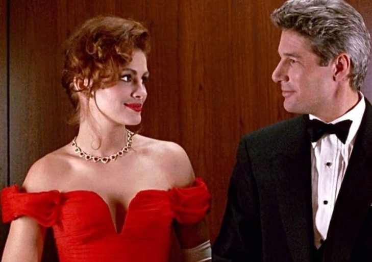 A still from 'Pretty Woman'. Edward and Vivian look at each other. She is wearing a bright red dress and he is wearing a smart suit.
