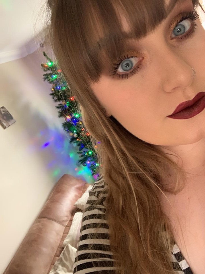 A young woman takes a selfie with a Christmas tree in the background.