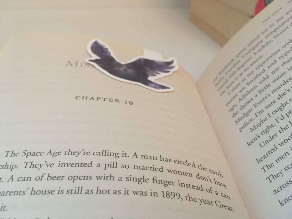 The open page of a book with a purple magnetic bird bookmark on the top of the page.