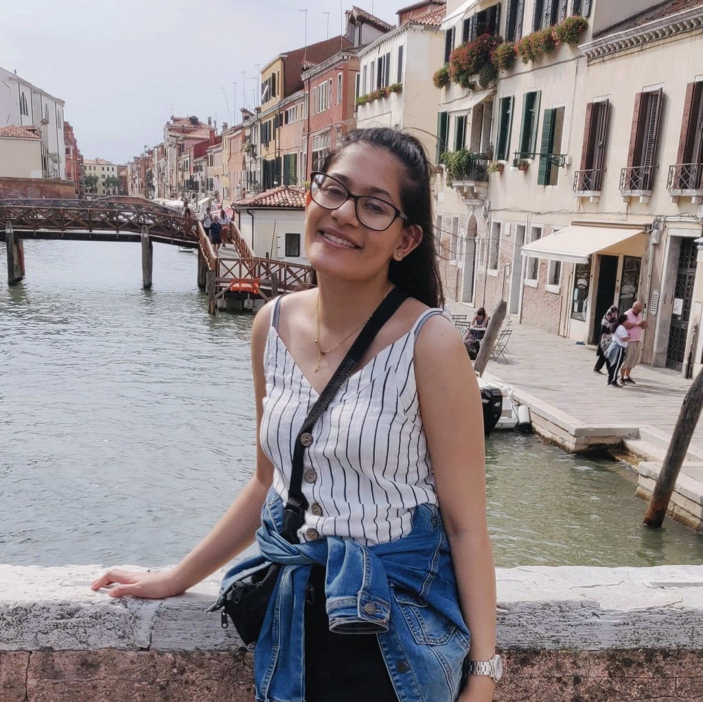 A young woman stands on a bridge and smiles for the camera.