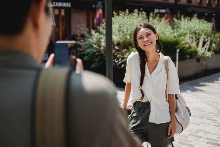 A man takes a photo of a woman while she poses and smiles.
