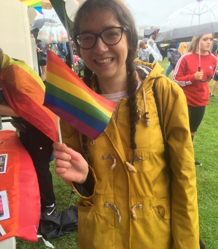 Young girl holds a Pride flag, wearing a bright yellow rain coat