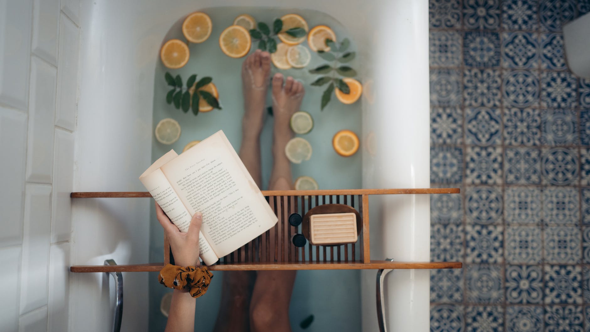 A woman lays in a luxurious bath, reading a book and surrounded by fresh fruit.