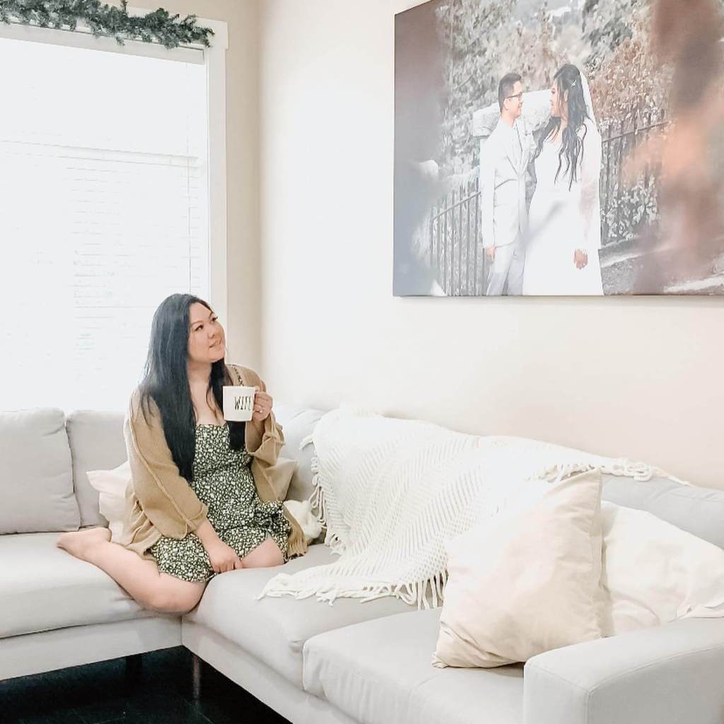 A woman sits on a grey sofa with a mug, looking at a picture from her wedding