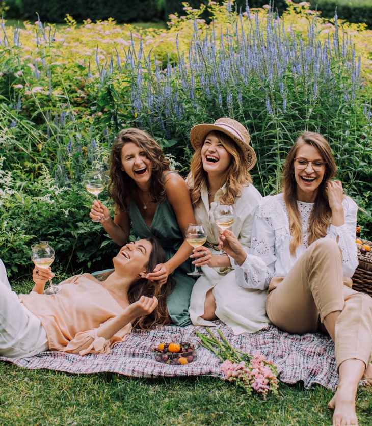 Four women laugh in a field with a picnic