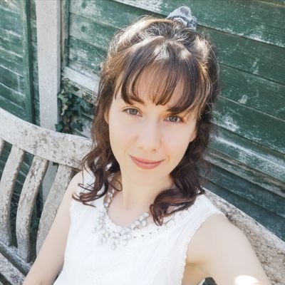 A young woman smiles at the camera, wearing a white dress