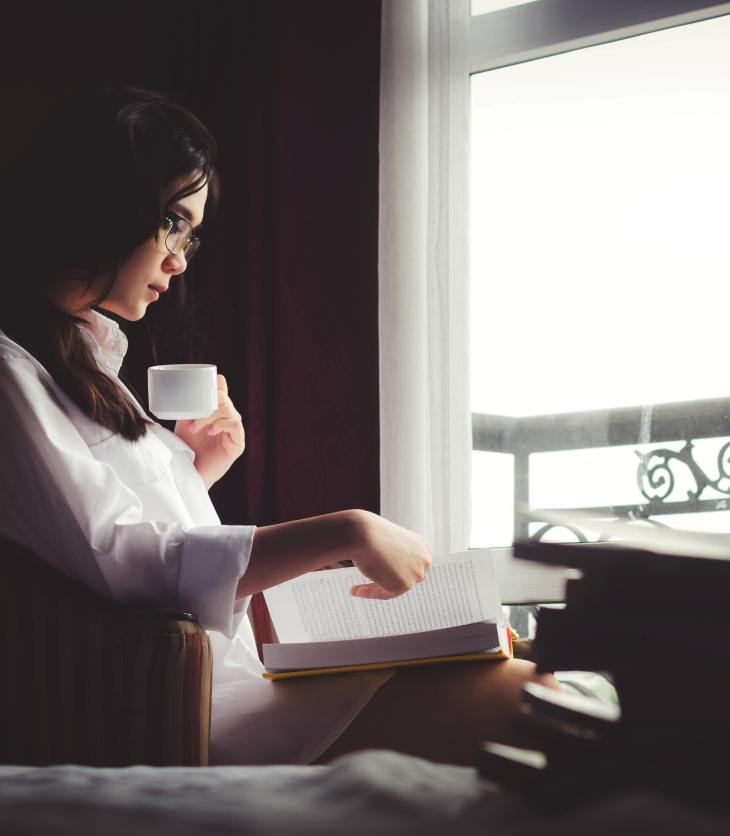 Woman reading alone by a window- spending time alone without feeling lonely