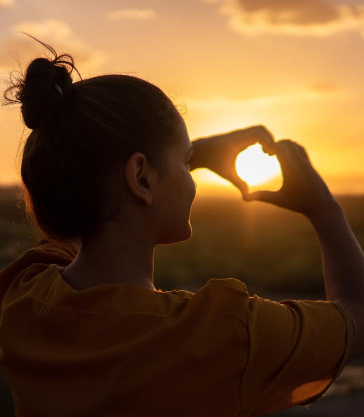 a woman signaling a heart with her hands at the sun, inspirational image- 5 ways to show the most important person in your life how much you love them