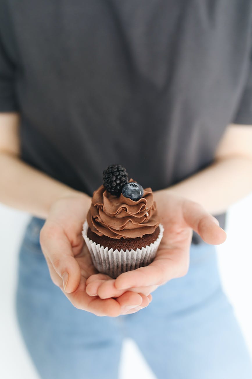 close up shot of a person holding a chocolate cupcake with berries on top- baking for Bake-Off