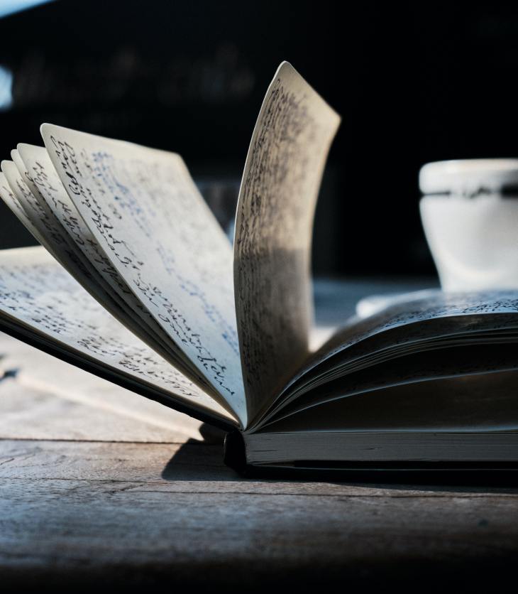 a notebook full of writing, with a teacup next to it