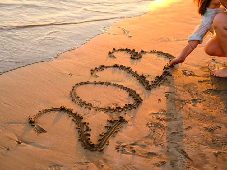 a woman writing 2023 on sand with her hand