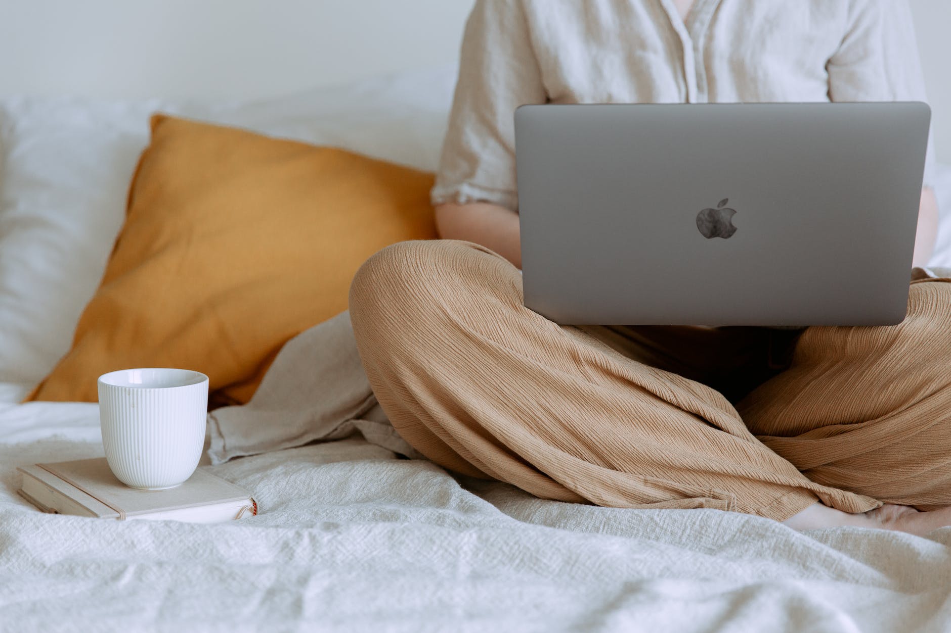 woman using laptop in bedroom with a mug and notebook
