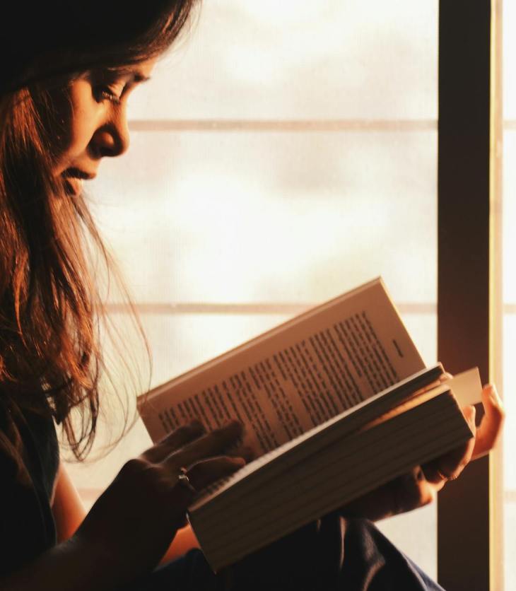 person reading a book beside the window