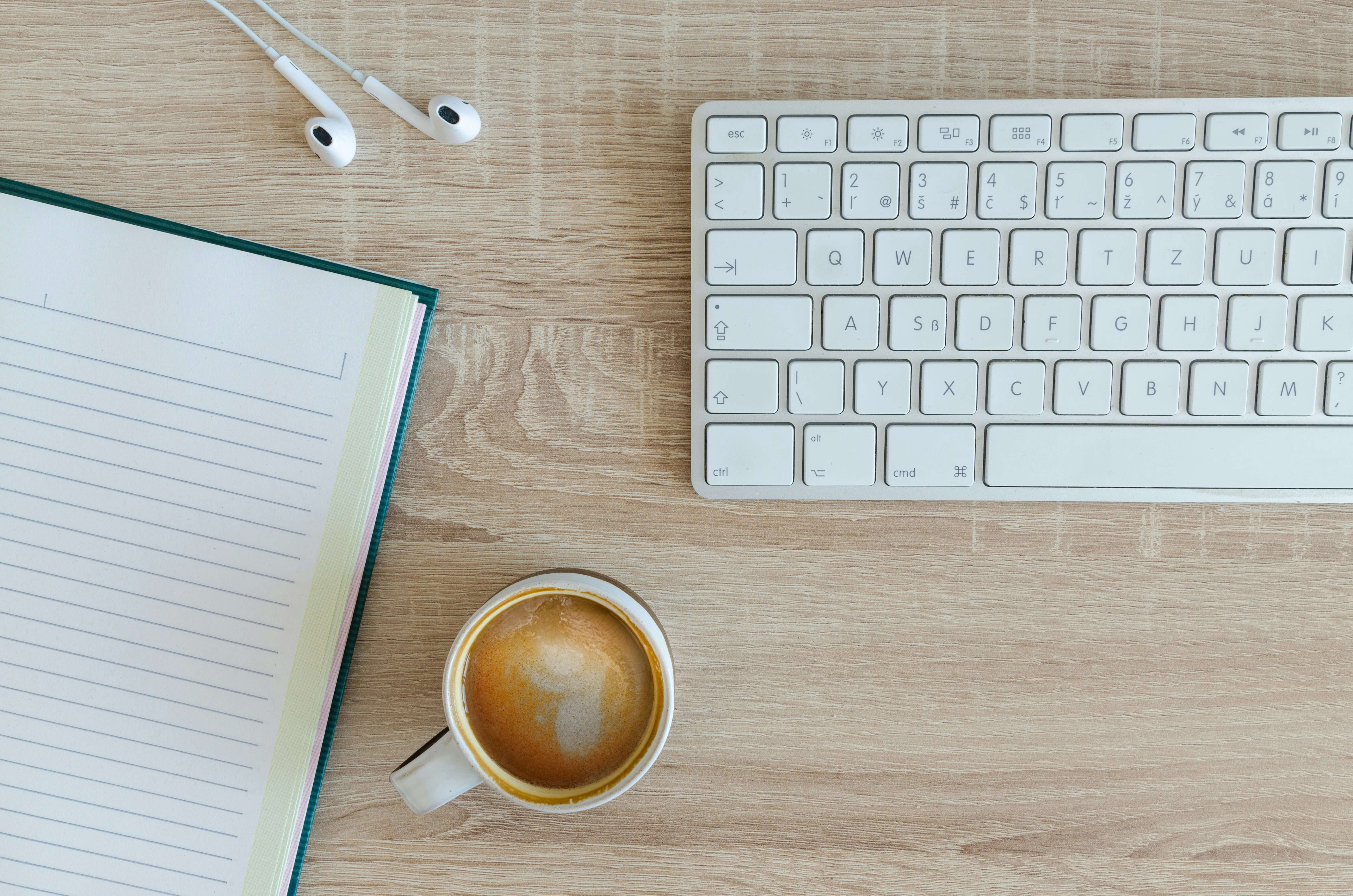 close up of a desk, including a keyboard, coffee mug, headphones and notebook: evening freelance routine