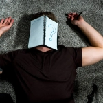 person laying on the floor with a notebook over the face