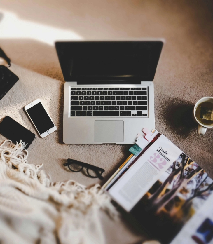laptop, open book, mug of tea, phones and blanket on the floor
