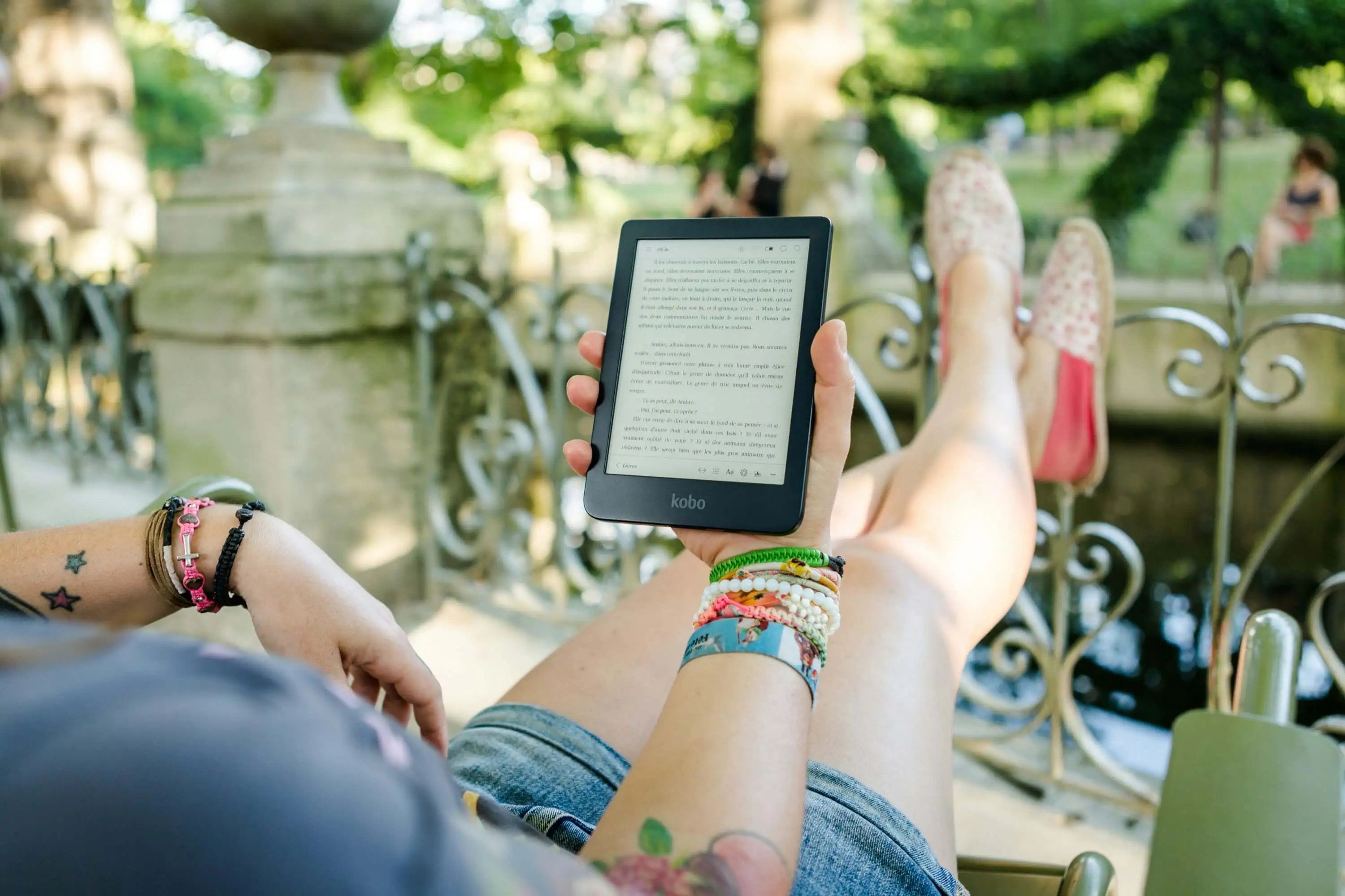 person in a seat outside with feet up reading an ebook on a Kindle screen: ebook ideas for creative freelancers