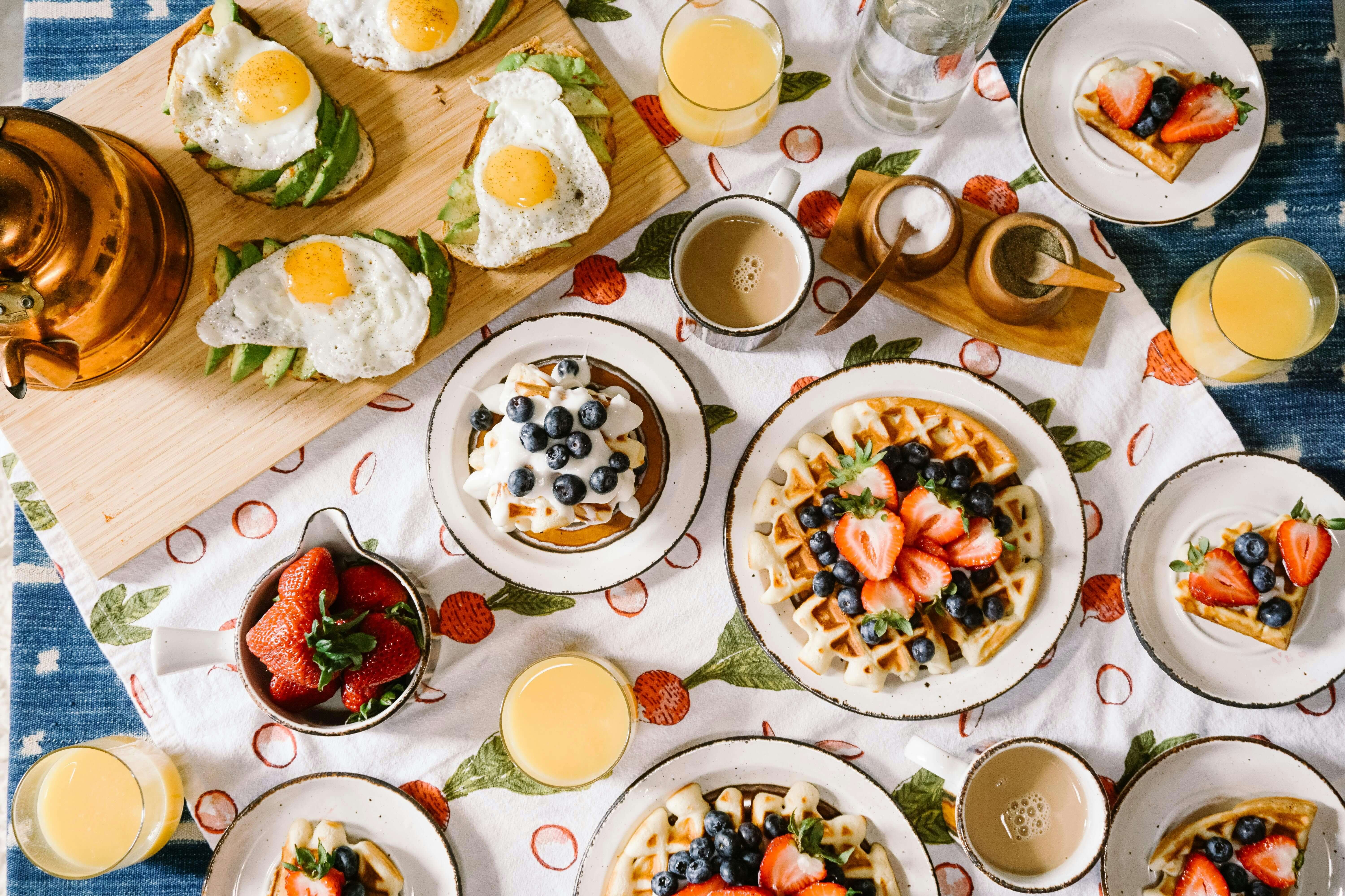a table with breakfast food and drinks like waffles, eggs, avocado and orange juice