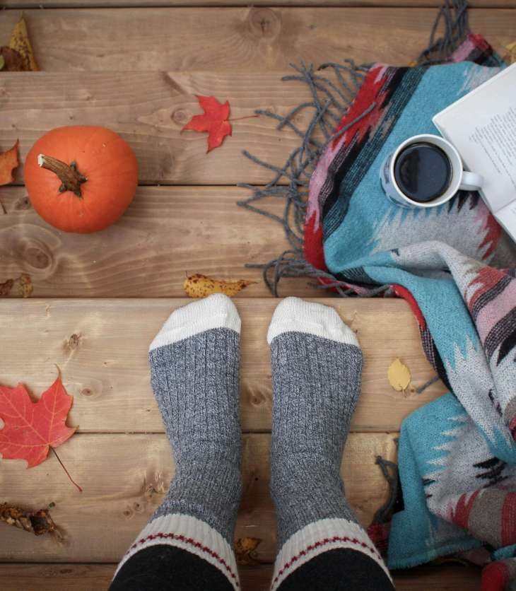 someone in cosy socks stood on a wooden floor with open book, mug, pumpkin and blanket