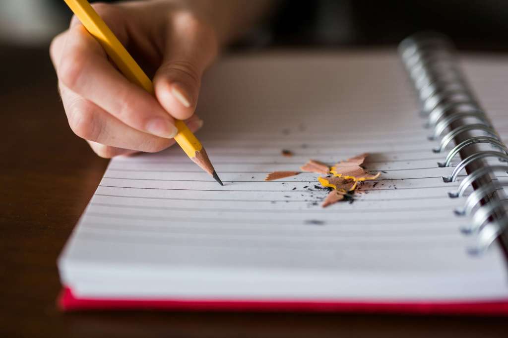 hand writing with a pencil in a lined notebook - pencil shavings on the page
