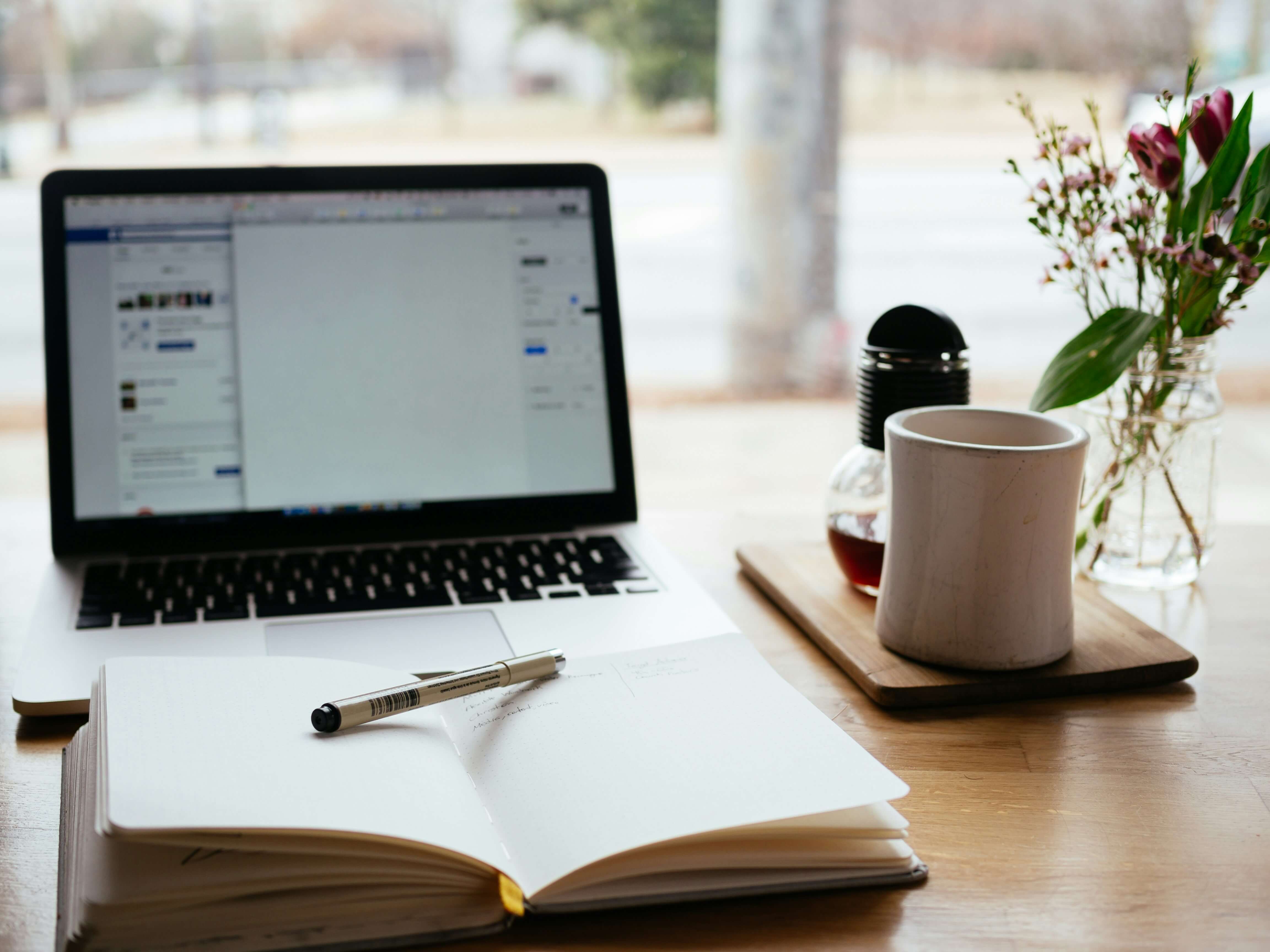 laptop, open notebook, plant in a vase and mug on a desk