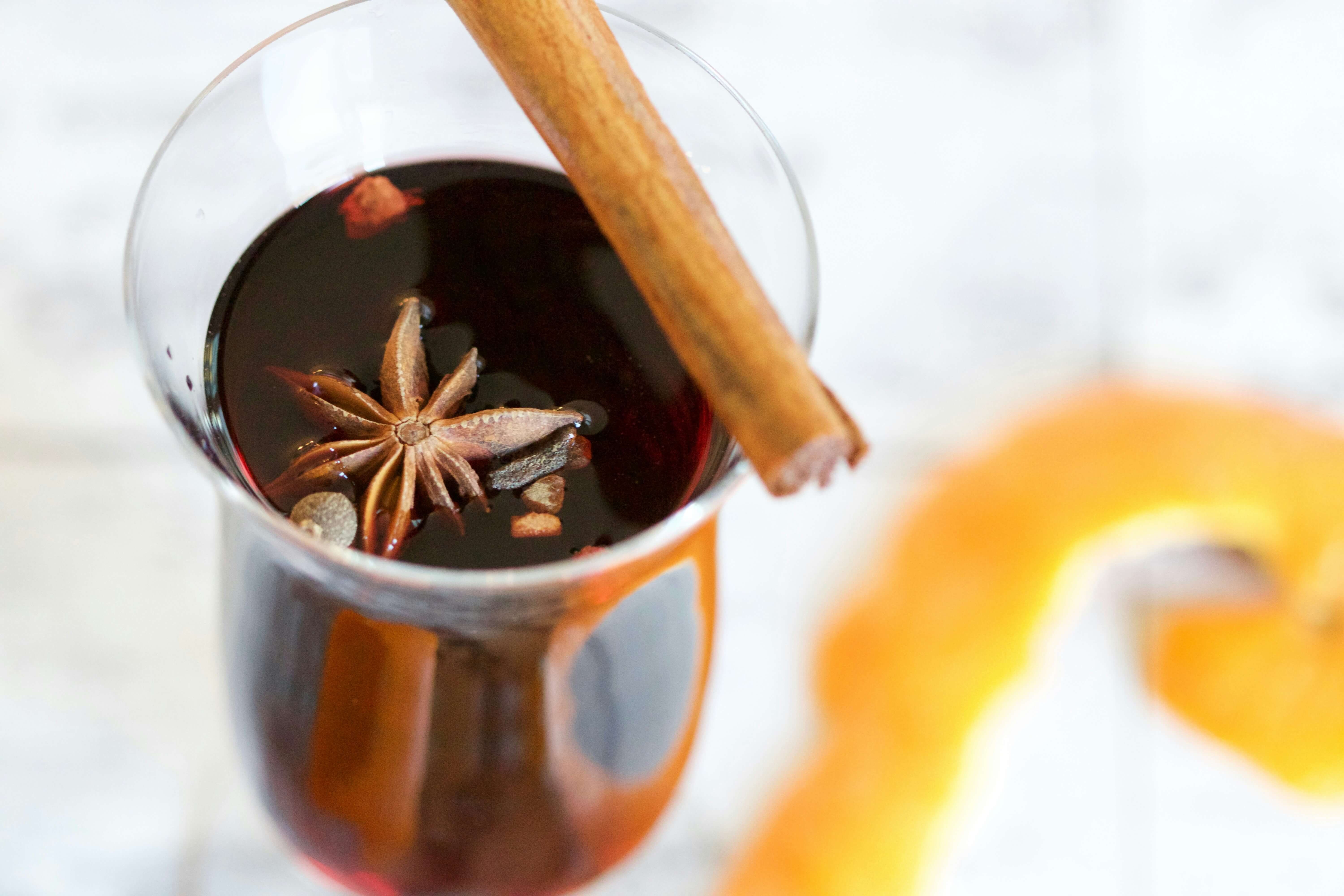 Christmas drink - glass of liquid with a cinnamon stick on top and orange peel in the background
