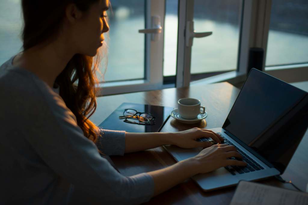 person typing at a laptop on a desk by French windows: how to write a good blog post
