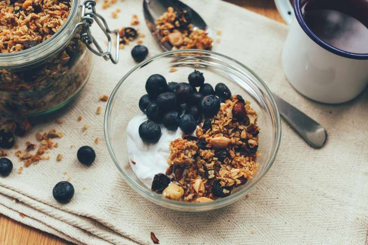 yoghurt and fruit and granola in a glass bowl with a jar of granola and a spoon next to it