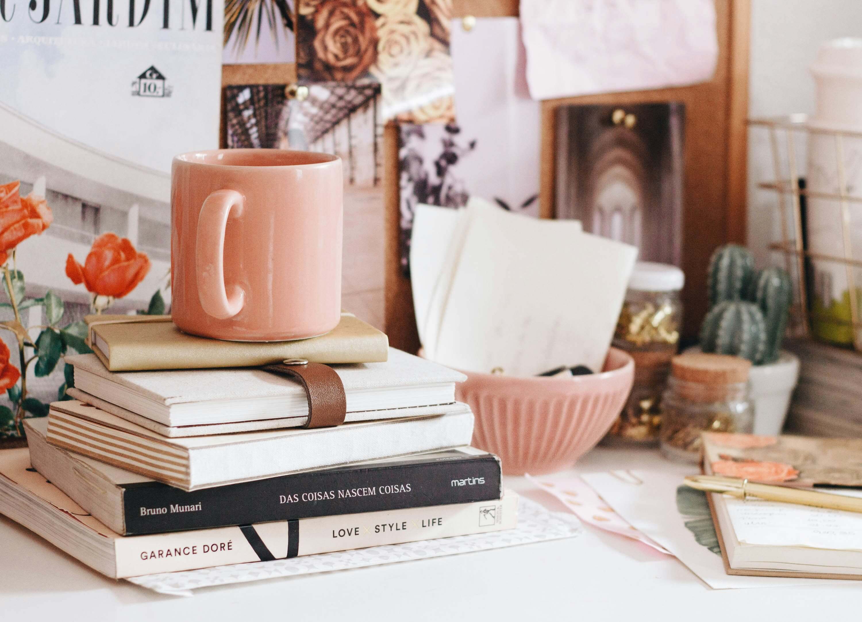 pile of books with a pink mug on top and lots of cute desk accessories