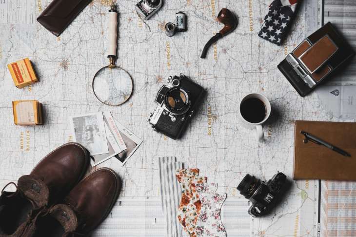 travel accessories like a camera, a magnifying glass, a mug of coffee and maps