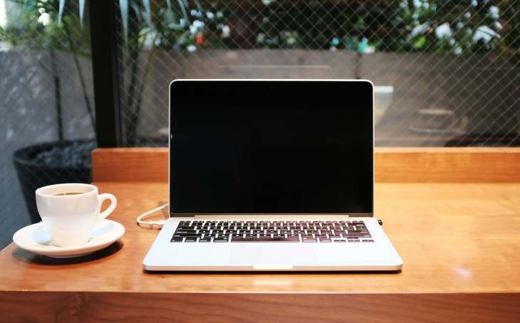laptop on a desk with a cup and saucer next to it