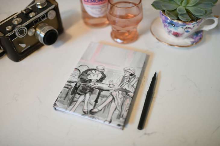 notebook, pen, camera, teacup with a plant in it, glass on a desk