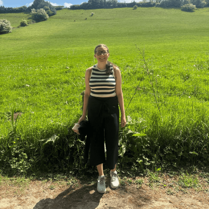 young woman standing in front of a field smiling