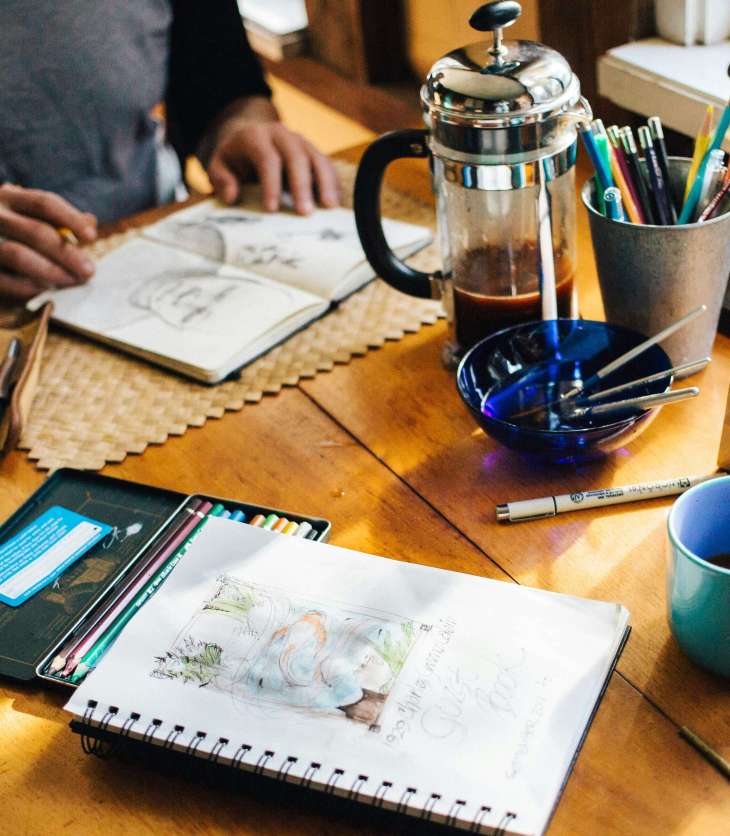 a table with sketchbooks, paints, coffee and other creative tools