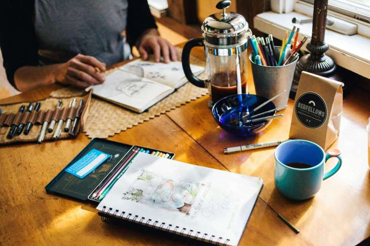 a table with sketchbooks, paints, coffee and other creative tools