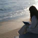 woman silhouette sitting on a beach reading
