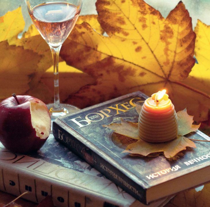 image of two books with autumn leaves, a wine glass, an apple with a bite out of it and a candle