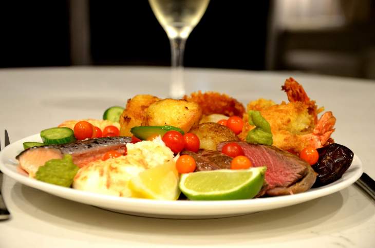 a plate of food, including meat and vegetables, with a glass of wine on a table - zoomed in on the plate of food