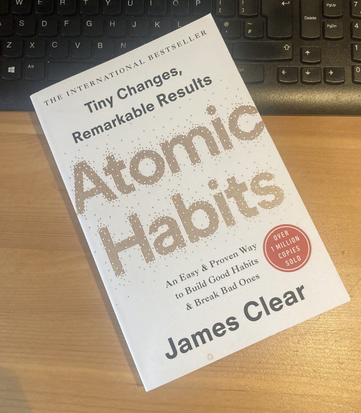 a copy of james clear' Atomic Habits laying on a desk and keyboard