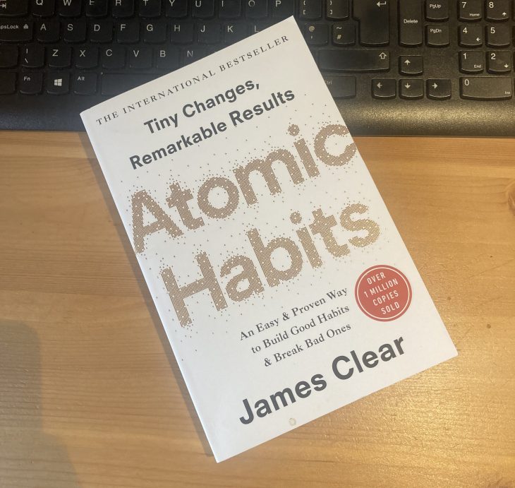 a copy of james clear' Atomic Habits laying on a desk and keyboard