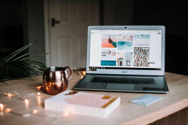 laptop on a desk with assorted things, such as a book and mug