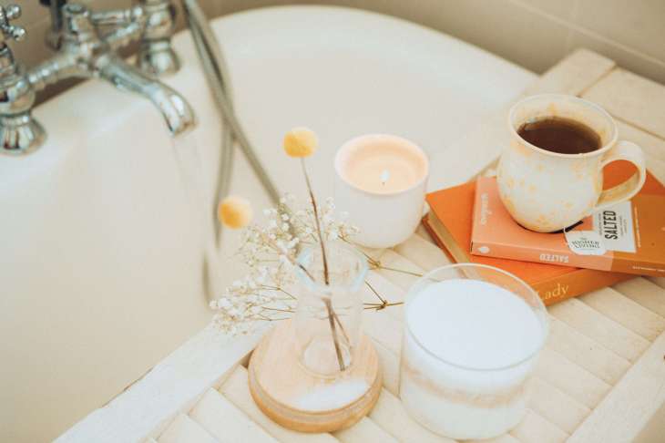 bath side with flowers, full mug, candles and two books piled under the mug