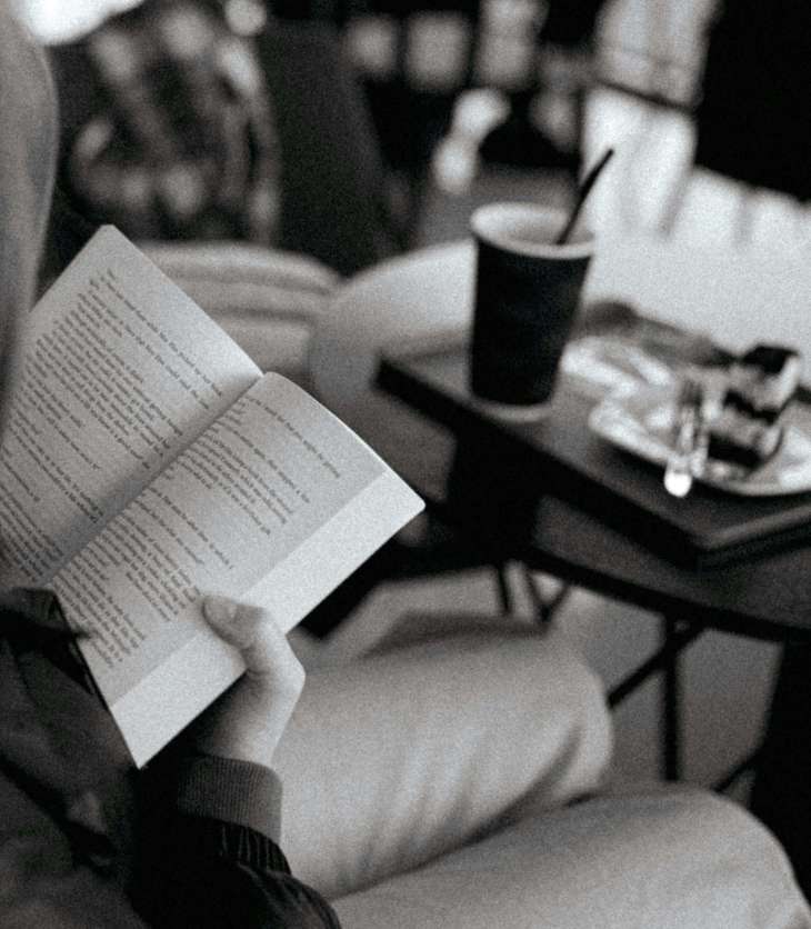 black and white image of someone reading a book in a cafe at a small table