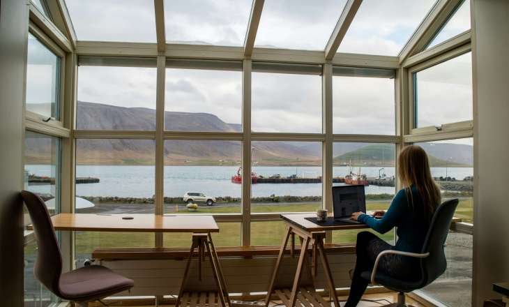 woman working with her back to the camera at a desk with a laptop - huge window in front of her with cliffs and body of water