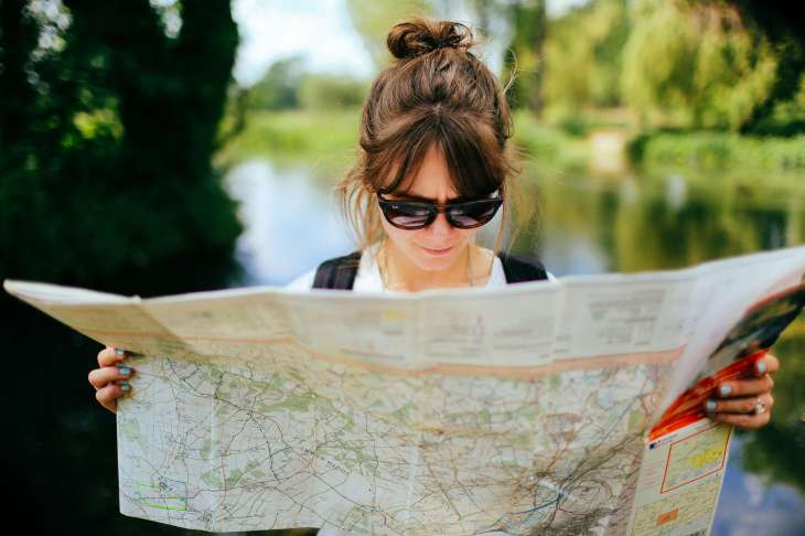 woman holding a big map with a body of water and trees behind her