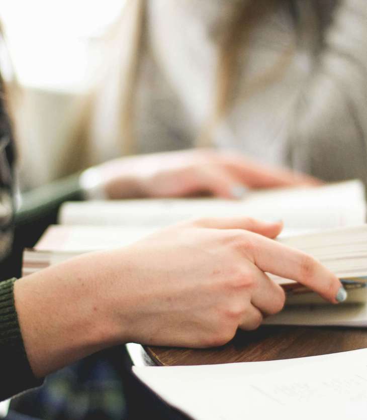 zoom in on hands holding a book on a desk with another person in the background