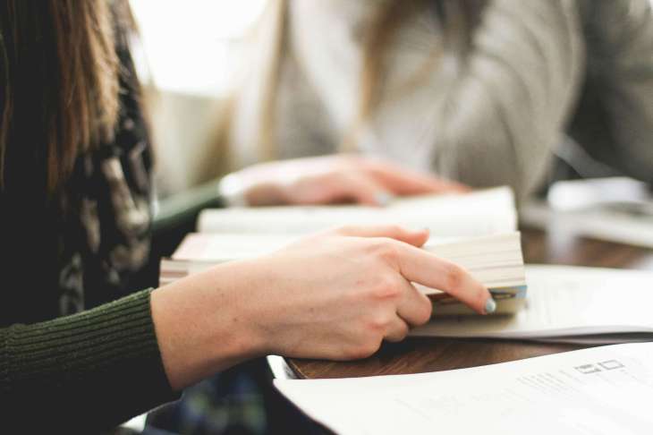 zoom in on hands holding a book on a desk with another person in the background