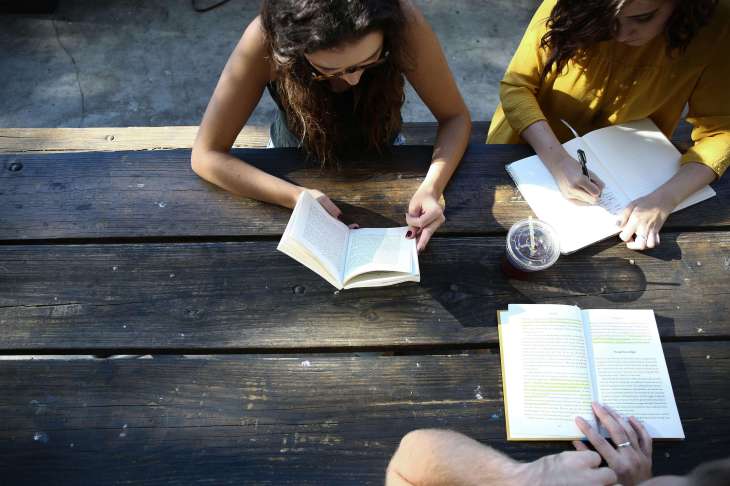 three people reading  books sat at a table books laid open on the table - bird's eye view of them