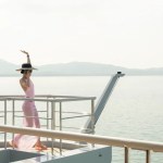 still from white lotus 3 - young woman on the edge of a yacht with her hand raised in the air, sea in the background